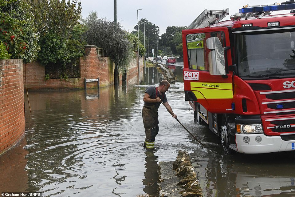 En brandmand fra Dorset og Wiltshire brandmandskab hjælper med at pumpe noget af vandet ud af vejen med deres brandbil efter voldsom regn og tordenvejr forårsagede lynoversvømmelser tirsdag