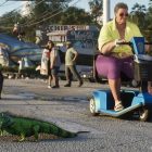 An iguana crossing a street near a woman on a scooter